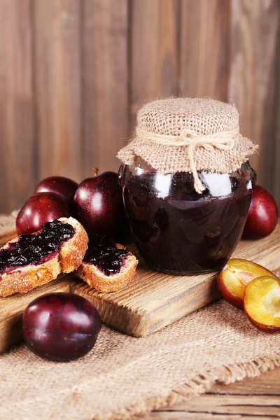 Sabrosa mermelada de ciruela en frasco y ciruelas en la mesa de madera de cerca — Foto de Stock