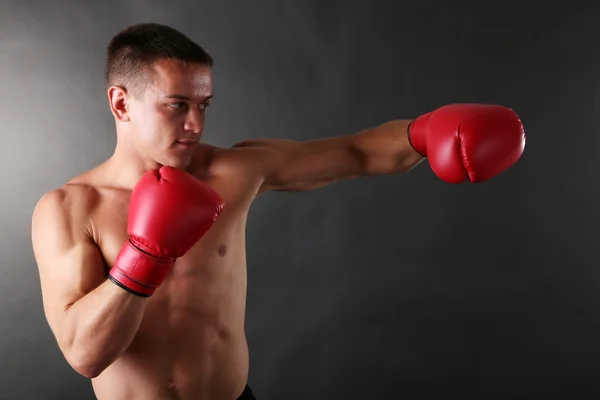 Bonito jovem desportista muscular com luvas de boxe no fundo escuro — Fotografia de Stock