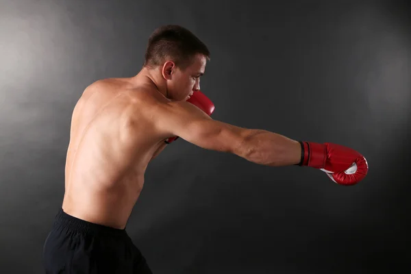 Bonito jovem desportista muscular com luvas de boxe no fundo escuro — Fotografia de Stock