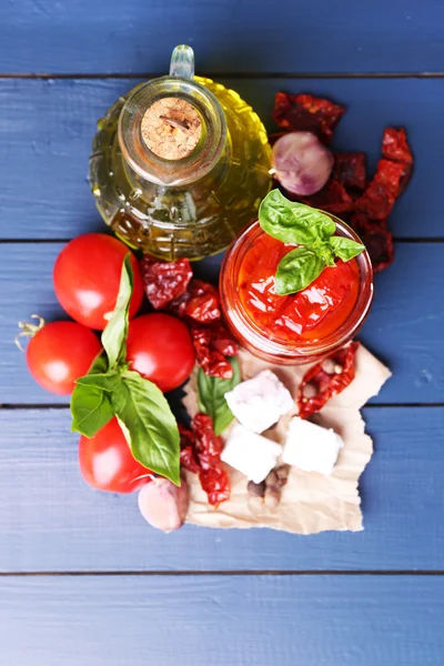 Tomates séchées au soleil dans un bocal en verre, huile d'olive en bouteille en verre et fromage feta sur fond en bois de couleur — Photo