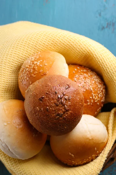 Tasty buns with sesame in wicker basket, on color wooden background — Stock Photo, Image