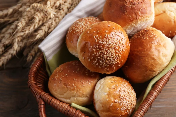 Tasty buns with sesame in wicker basket, on  wooden background — Stock Photo, Image