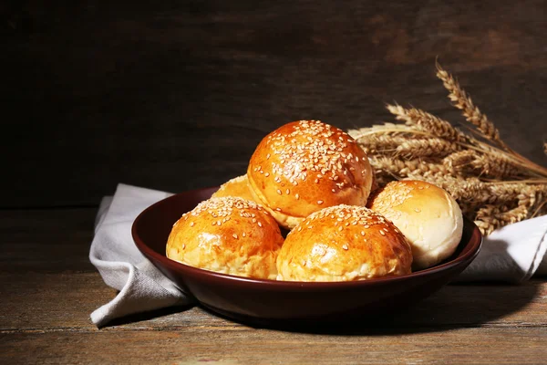 Tasty buns with sesame on plate, on wooden background — Stock Photo, Image