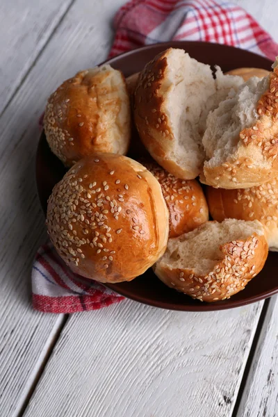 Petits pains savoureux au sésame sur assiette, sur fond de bois couleur — Photo