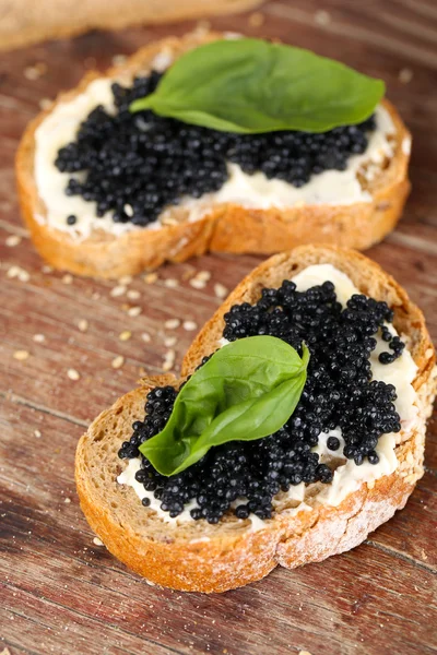 Slices of bread with butter and black caviar on wooden background — Stock Photo, Image