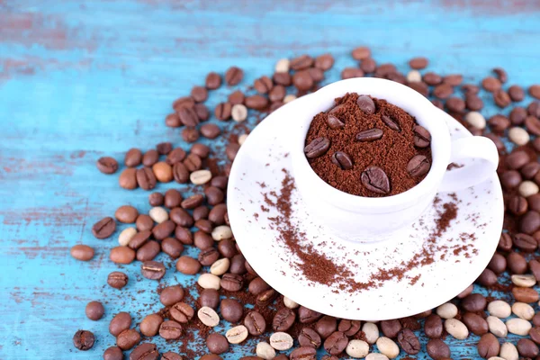 Kaffeebohnen in weißer Keramiktasse mit Untertasse auf blauem Holzhintergrund — Stockfoto