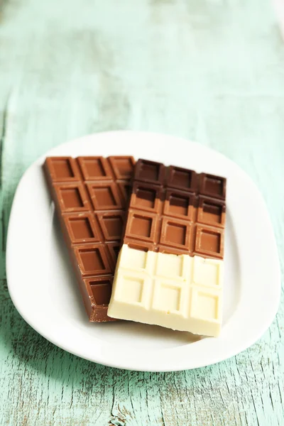 Chocolate bars on plate on wooden background — Stock Photo, Image