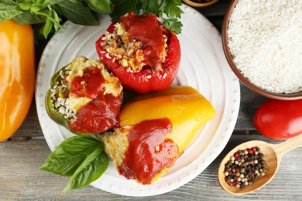 Composição com pimentas recheadas preparadas em prato e ervas frescas, especiarias e legumes, sobre fundo de madeira — Fotografia de Stock