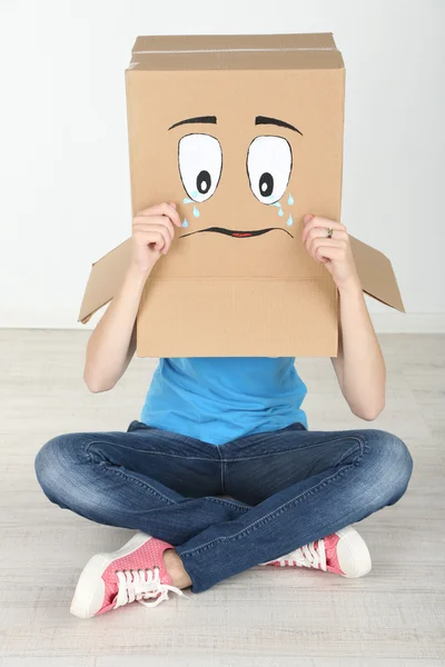 Femme avec boîte en carton sur la tête avec visage triste, près du mur — Photo