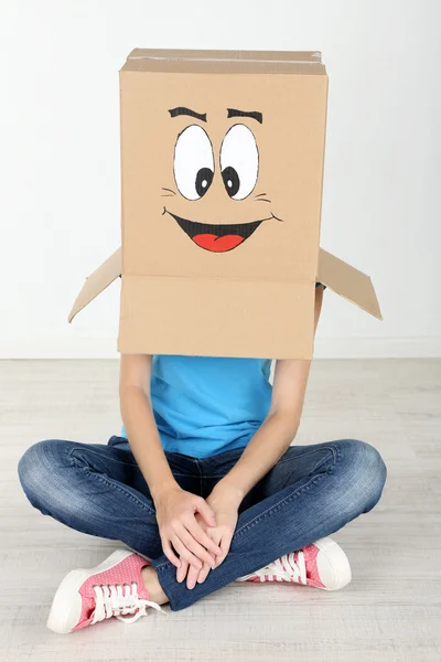 Mulher com caixa de papelão na cabeça com rosto feliz perto da parede — Fotografia de Stock