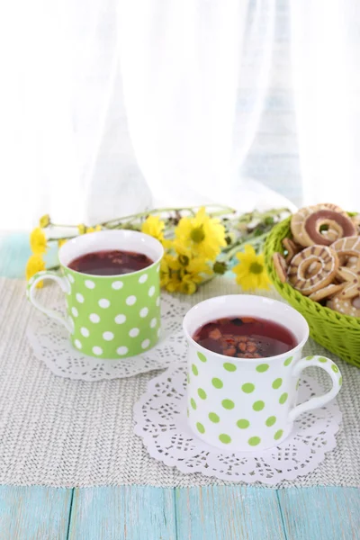 Two polka dot cups of tea with biscuits on table on curtain background