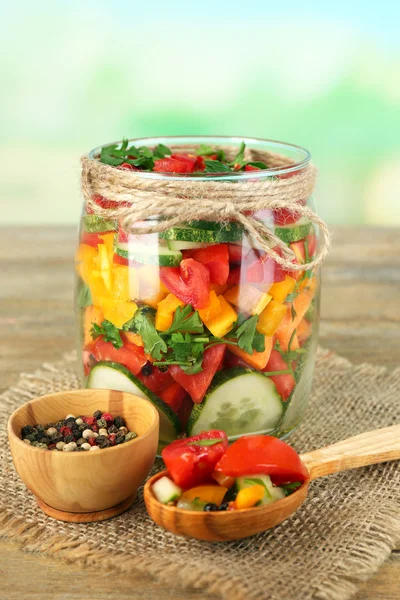 Plantaardige salade in glazen pot, op zak servet, op houten tafel, op lichte achtergrond — Stockfoto