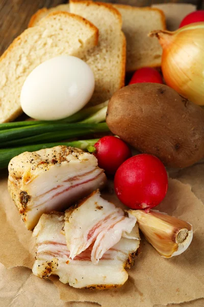 Bacon, färska grönsaker, kokt ägg och bröd på papper, på trä bakgrund. Frukostkoncept i byn. — Stockfoto