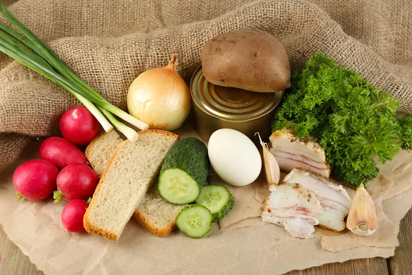 Bacon, färska grönsaker, kokt ägg och bröd på papper, på trä bakgrund. Frukostkoncept i byn. — Stockfoto