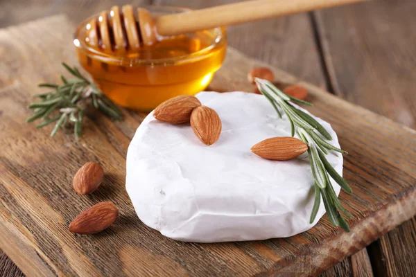 Camembert cheese, honey in glass bowl and nuts on cutting board on wooden background — Stock Photo, Image