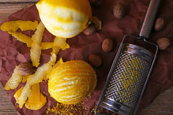 Lemons, nutmegs and grater on paper on wooden background — Stock Photo, Image
