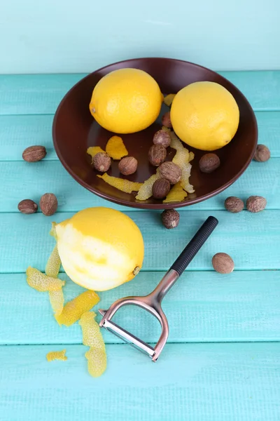 Ripe lemons and nutmegs on plate and half peeled lemon with peeling knife on blue wooden background — Stock Photo, Image