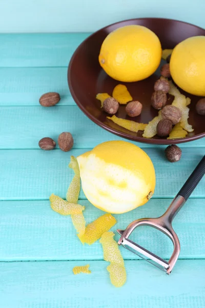 Limones maduros y nueces en plato y limón medio pelado con cuchillo pelador sobre fondo de madera azul —  Fotos de Stock