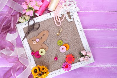 Scrapbooking craft materials and wooden frame with sackcloth inside on color wooden background clipart