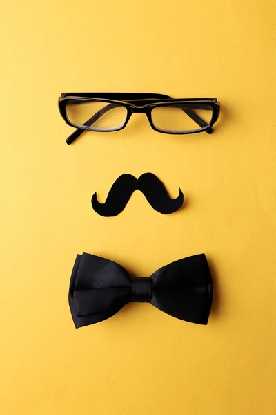 Glasses, mustache and bow tie forming man face on yellow background — Stock Photo, Image