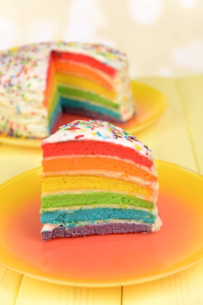 Köstlicher Regenbogenkuchen auf Teller auf Tisch vor hellem Hintergrund — Stockfoto