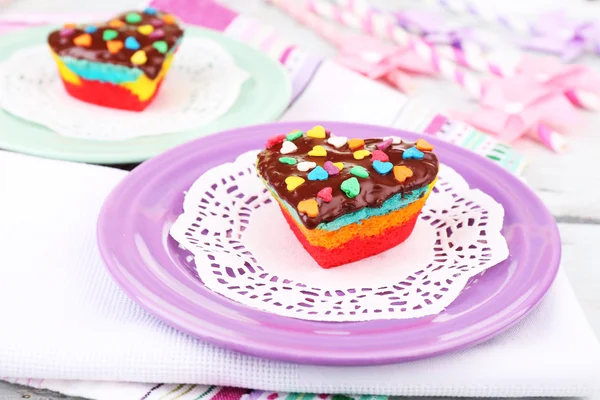 Deliciosos pasteles de arco iris en platos, sobre fondo de madera de color —  Fotos de Stock