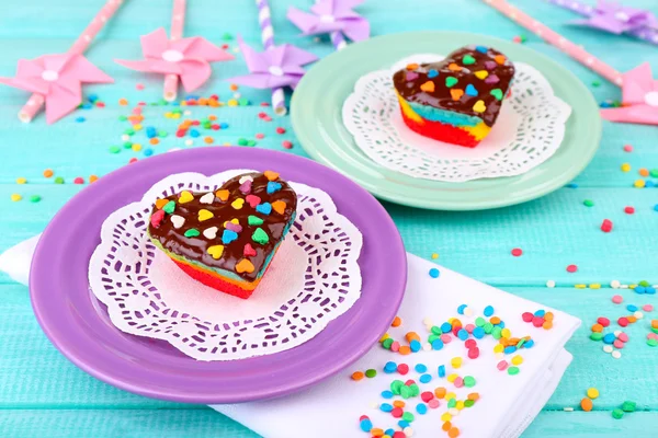 Deliciosos pasteles de arco iris en platos, sobre fondo de madera de color —  Fotos de Stock