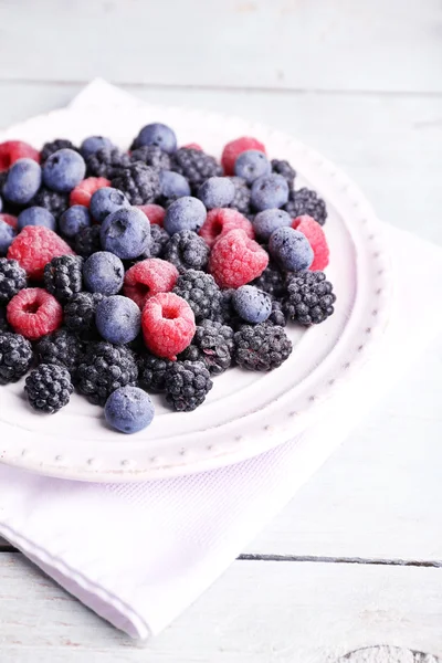 Ледяные ягоды на тарелке, на цветном деревянном фоне — стоковое фото