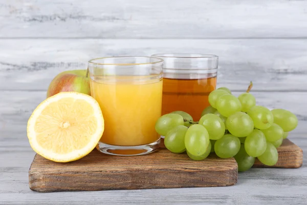 Ποτήρια χυμό με φρέσκα φρούτα στο γκρι ξύλινο τραπέζι — Φωτογραφία Αρχείου