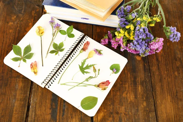 Samenstelling met bloemen en droog van planten op notebook op houten achtergrond — Stockfoto