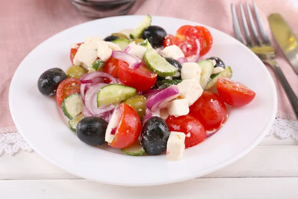 Greek salad served in plate on napkin on wooden background — Stock Photo, Image