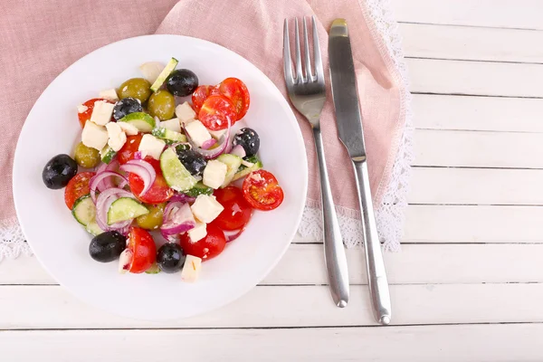 Greek salad served in plate on napkin on wooden background — Stock Photo, Image