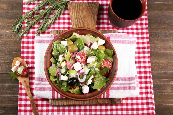 Ciotola di insalata greca servita sul tagliere tovagliolo su tavolo di legno su sfondo scuro — Foto Stock