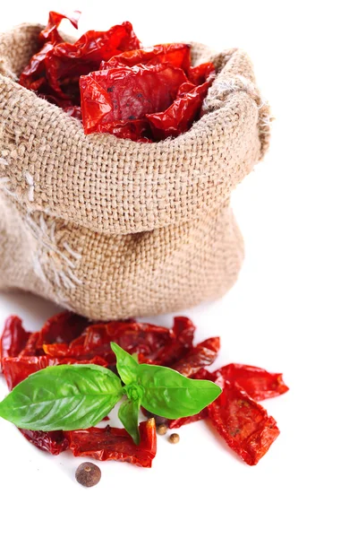 Sun dried tomatoes in sackcloth bag and basil leaves, isolated on white — Stock Photo, Image
