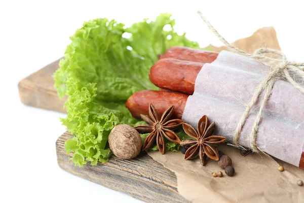 Salsichas finas defumadas com folhas de salada de alface e especiarias em tábua de corte de madeira, isoladas em branco — Fotografia de Stock