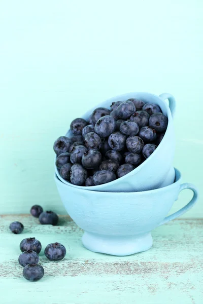 Bleuets mûrs savoureux dans des tasses, sur une table en bois — Photo