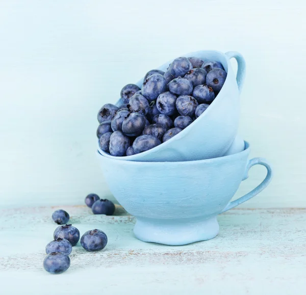 Läckra mogna blåbär i koppar, på träbord — Stockfoto