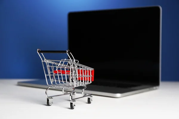 Carro de la compra en el ordenador portátil en la mesa, sobre fondo azul Imagen De Stock