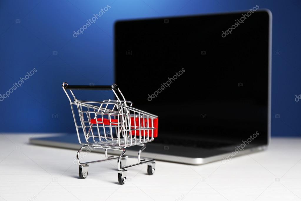 Shopping cart on laptop on table, on blue background