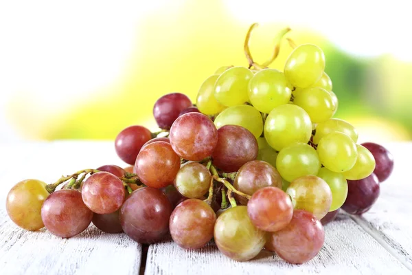 Bunches of ripe grapes on wooden table on natural background — Stock Photo, Image