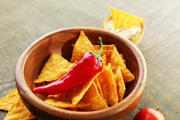 Nachos saborosos, tomates vermelhos e pimenta na tigela de cor no fundo de madeira — Fotografia de Stock