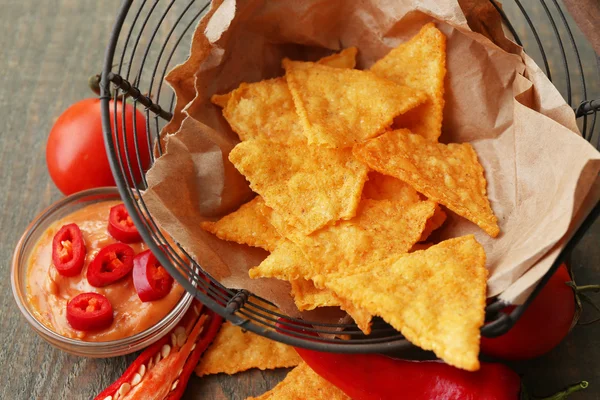 Nachos saborosos, tomates vermelhos e pimenta em cesta no fundo de madeira — Fotografia de Stock