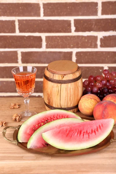 Composizione di anguria matura, frutta, vino rosa in vetro e botte di legno sul tavolo di legno di colore, su sfondo mattoni — Foto Stock