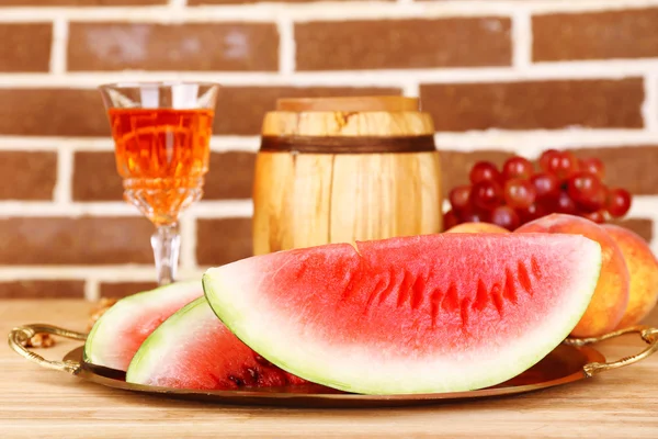 Composizione di anguria matura, frutta, vino rosa in vetro e botte di legno sul tavolo di legno di colore, su sfondo mattoni — Foto Stock