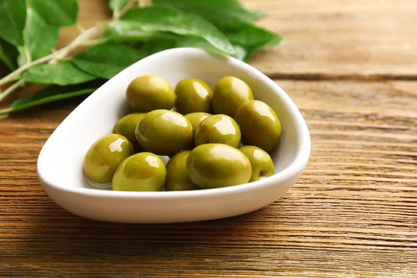 Green olives in bowl with leaves on table close-up — Stock Photo, Image