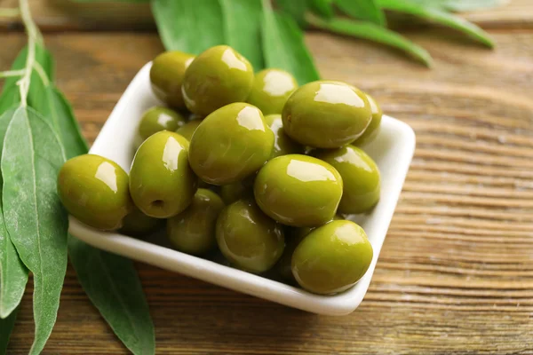 Grüne Oliven in Schüssel mit Blättern auf dem Tisch in Großaufnahme — Stockfoto