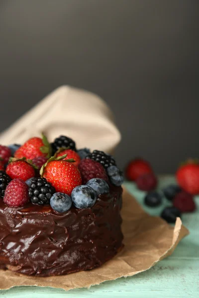 Tasty chocolate cake with different berries on wooden table, on dark background — Stock Photo, Image