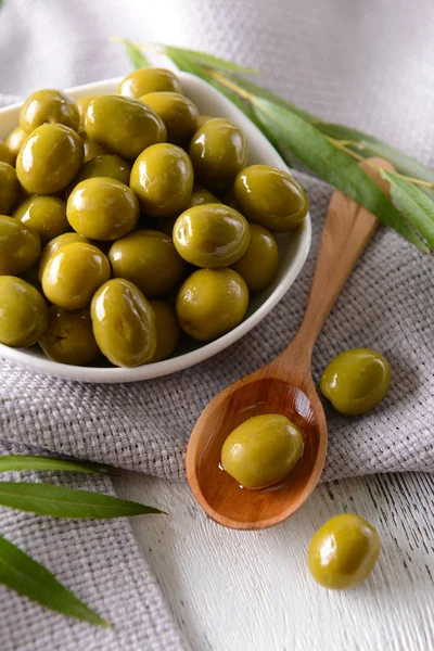 Green olives in bowl with leaves on table close-up — Stock Photo, Image