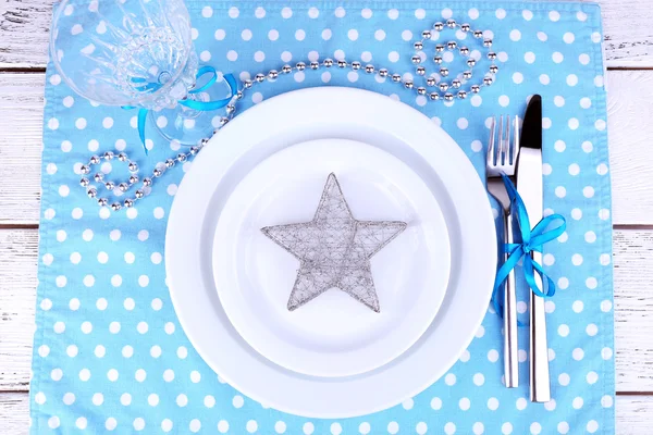 Белая тарелка, вилка, нож и рождественское украшение на салфетке в горошек на деревянном фоне — стоковое фото