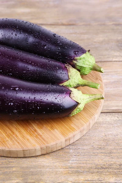 Aubergines on round cutting board on wooden background — Stock Photo, Image